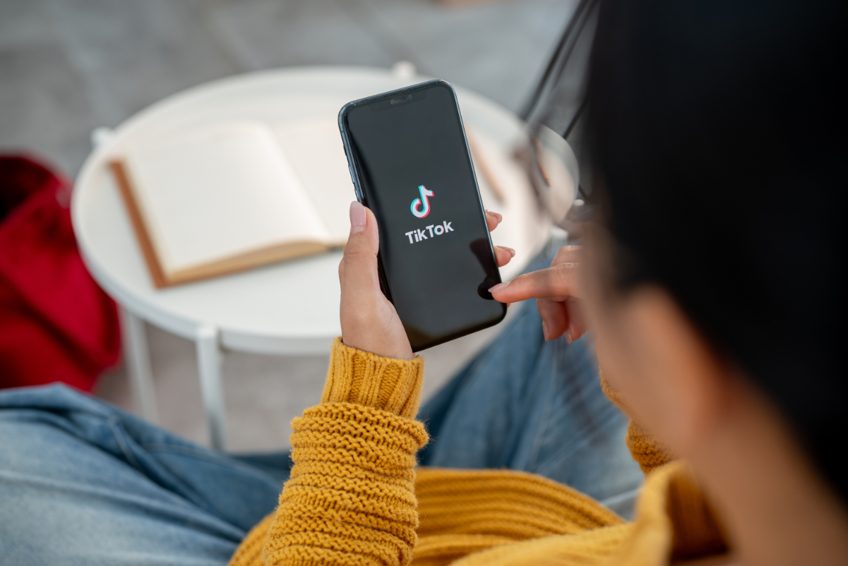 A close-up of a woman using the TikTok application on her iPhone while sitting on a couch at home.