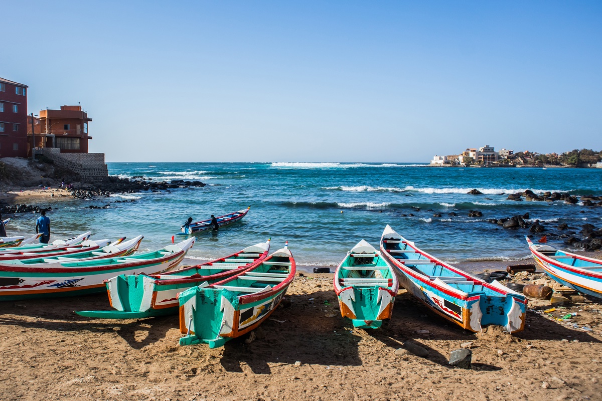 Boats lined up along a beach with the ocean behind them.